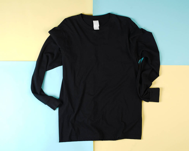 Pile of black folded clothes. Top view of folded black t-shirt isolated with colored background, copy space, flat lay. Blank t-shirt templates are commonly used for mockups and template designs. - Foto, imagen