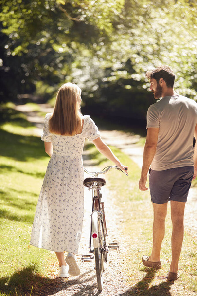 Rear View Of Couple Walking Along Summer Countryside Path Pushing Bike - 写真・画像
