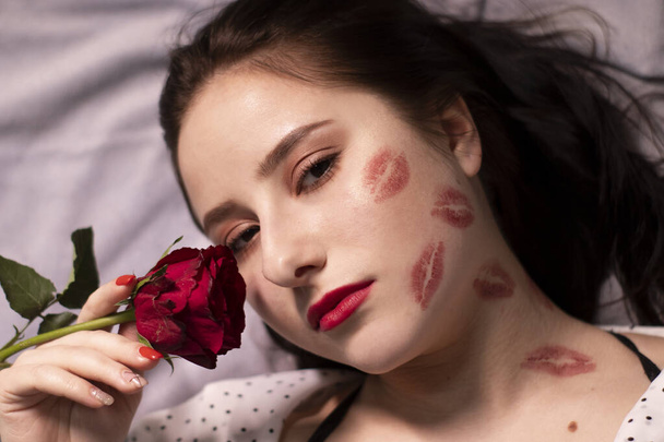 mulher morena sexy com beijos, marcas de batom em seu rosto e pescoço, com rosa vermelha. Namorada, encontro, relançamento. espaço de cópia - Foto, Imagem