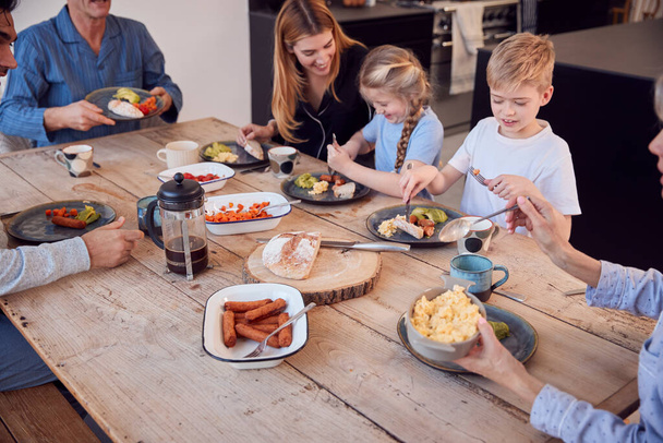 Multi-Generation Family Sitting Around Table At Home In Pyjamas Enjoying Brunch Together - 写真・画像