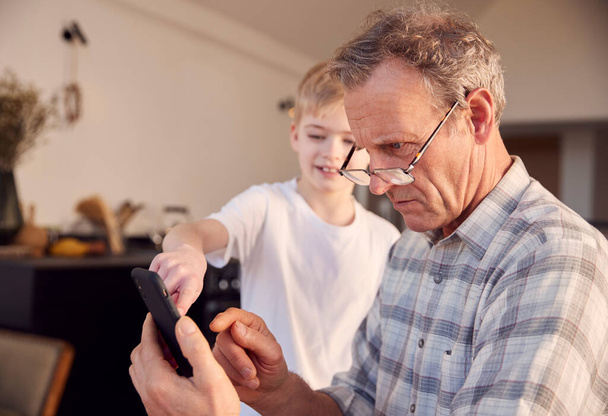 Grandson Showing Grandfather How To Solve Problem And Use Mobile Phone At Home - Foto, immagini