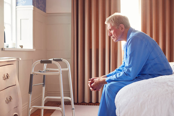 Unhappy And Depressed Senior Man Sitting On Edge Of Bed At Home During Lockdown For Covid-19 - Photo, Image