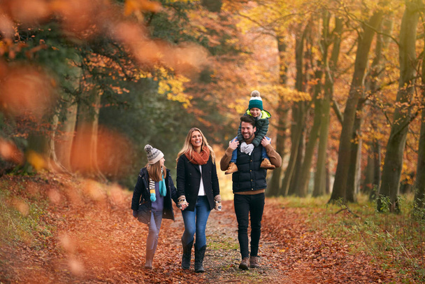 Family Walking Along Autumn Woodland Path With Father Carrying Son On Shoulders - Foto, Imagen