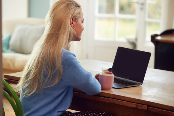 Задний вид женщины, сидящей за столом с ноутбуком, имеющей видео-чат с другом дома - Фото, изображение