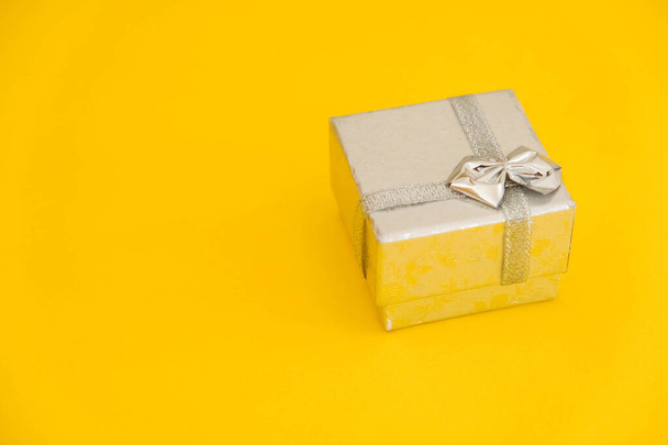 Zilverkleurige geschenkdoos op gele achtergrond. Kopieer, lege ruimte voor tekst. - Foto, afbeelding
