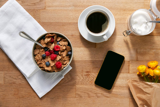 Kahvaltınız için gevrek ve kahveyle hazırlanmış cep telefonunuz masanın üzerinde. - Fotoğraf, Görsel