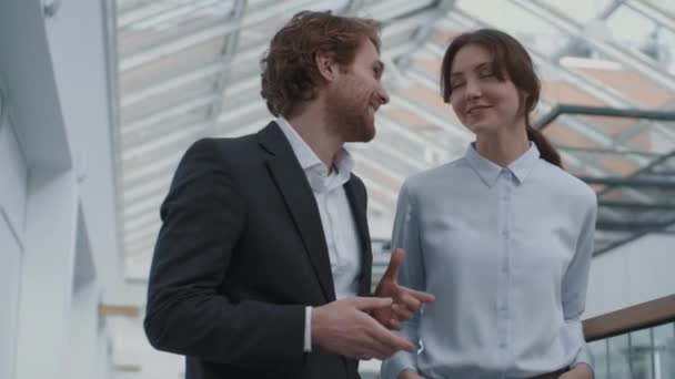 Medium shot of young Caucasian businesswoman and her young male colleague both wearing office wear going together along business center hall and having communication - Footage, Video