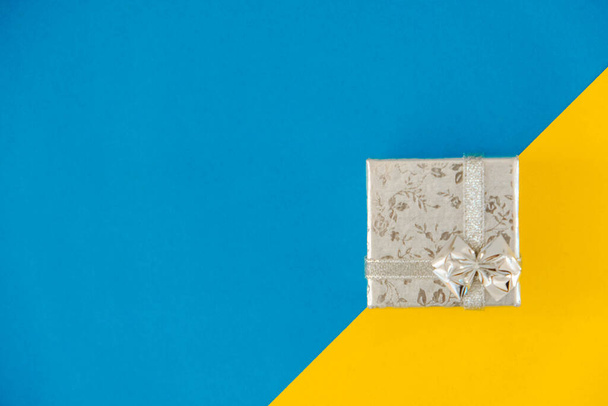 Mavi ve sarı arka planda gümüş hediye kutusu. Üst Manzara. Kopyala, metin için boşluk. - Fotoğraf, Görsel