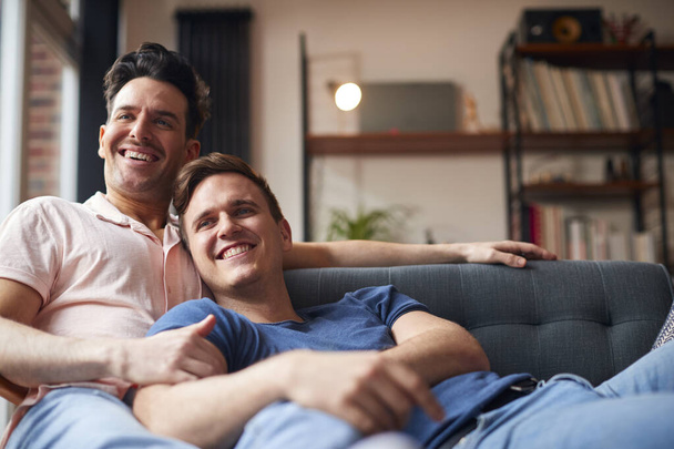 Loving Same Sex Male Couple Lying On Sofa At Home Watching TV And Relaxing Together - Zdjęcie, obraz