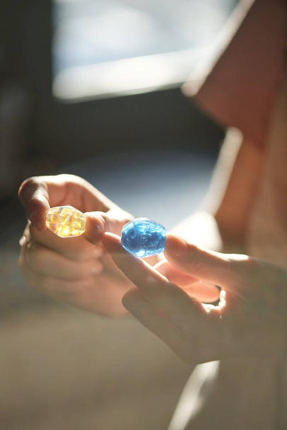 Manos de joven artesana sosteniendo azul y amarillos cuentas de vidrio hechas a mano mientras decide qué color elegir para el nuevo collar - Foto, Imagen