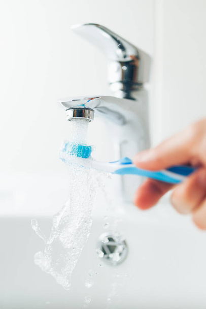 hand holding toothbrush under flowing water from faucet - Photo, image