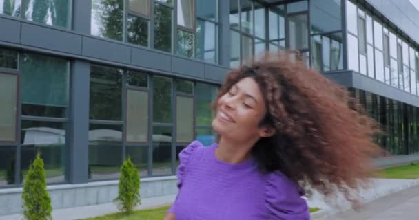 mujer emocionada sonriendo y fijando el pelo rizado cerca de la construcción  - Metraje, vídeo