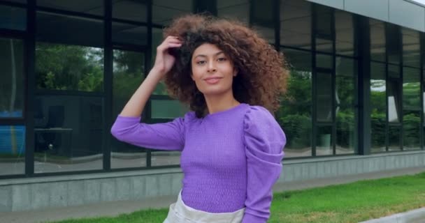 happy woman smiling and adjusting curly hair near building  - Footage, Video