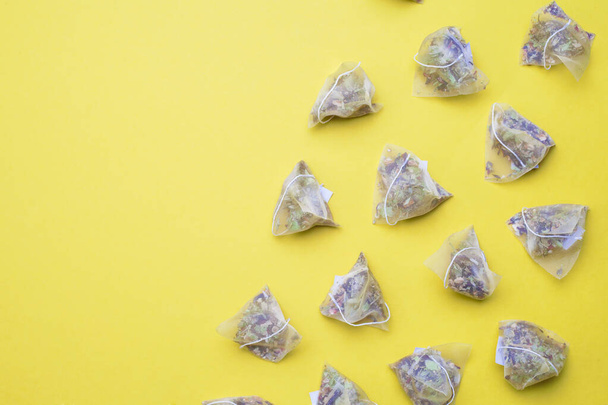 Плоский набор травяных чайных пирамид на пастельно-желтой поверхности. - Фото, изображение