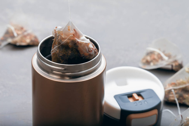 Tea bag in the shape of a pyramid on a gray background. Brew tea in a thermo mug - Photo, Image