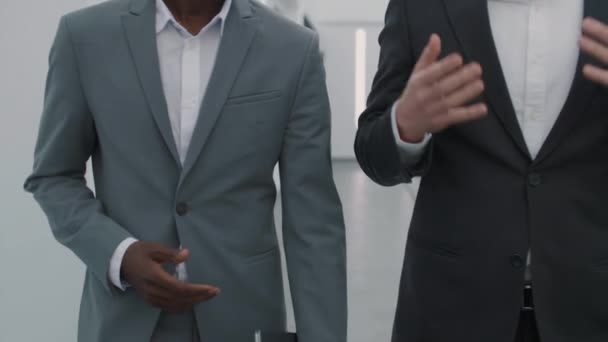 Medium shot van een paar verschillende onherkenbare zakenmannen dragen pakken gaan samen langs business center hal en hebben een gesprek - Video