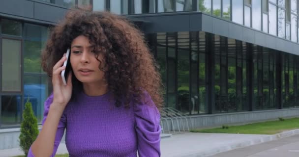 curly woman quarrelling while talking on smartphone outside - Footage, Video