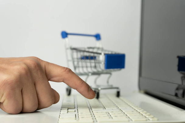 Online shopping concept.Man hand using laptop with mini shopping cart on white background.Business financial spend money lifestyle.Work from home background. - Photo, Image