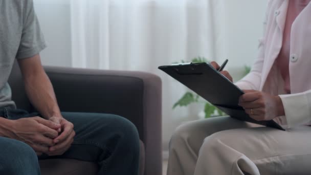 A man is discussing a problem with a psychiatrist. The psychiatrist is note a detailed breakdown of the symptoms and putting them on the male's legs for encouragement. A mentor's concept of stress and mental symptoms - Footage, Video