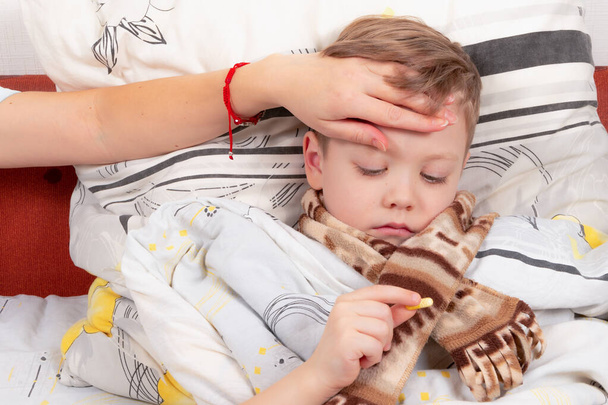 Kisfiú gyermek csomagolva egy sál beteg otthon, fekszik az ágyban, és iszik gyógyszert - Fotó, kép