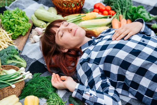 Portrait beautiful woman with closed eyes lying on a plaid among fresh organic vegetables. Top view. Copy, empty space for text. - Photo, Image