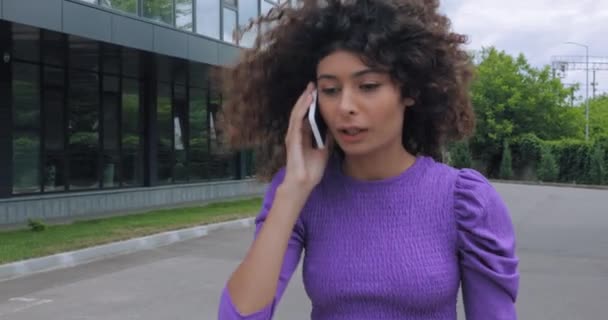 χαμογελαστή νεαρή γυναίκα που μιλάει στο smartphone κοντά στο κτίριο  - Πλάνα, βίντεο