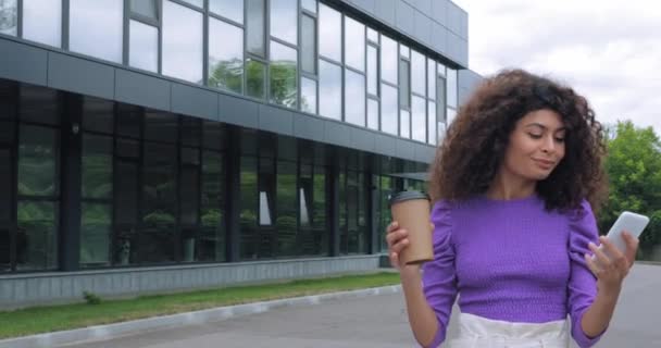 χαρούμενη γυναίκα πίνοντας καφέ για να πάει και να χρησιμοποιήσει το smartphone έξω  - Πλάνα, βίντεο