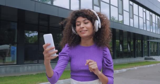 happy young woman in wireless headphones having video call outside  - Footage, Video
