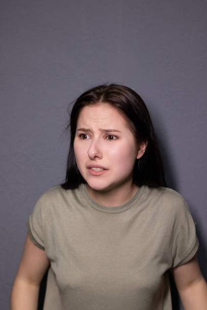 portrait of charming scared brunette woman in marsh color t-shirt on grey wall background. actress acting, emotion. copy space - 写真・画像