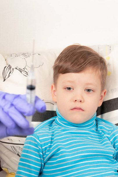 ένας γιατρός με μπλε ιατρικά γάντια εγχέει ένα άρρωστο παιδί με μια σύριγγα - Φωτογραφία, εικόνα