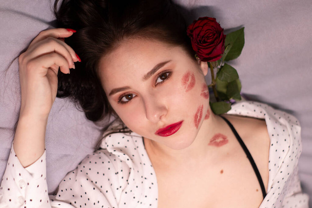 sexy brunette vrouw met kussen, lippenstift markeringen op haar gezicht en nek, met rode roos. vriendin, afspraakje, relatieperiode. kopieerruimte - Foto, afbeelding