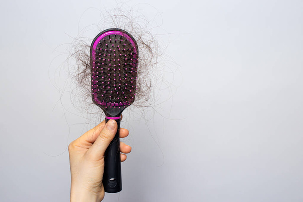 The girl is holding a hairbrush with lost hair. Hair loss, care and treatment. Trichologist, trichology. Banner with place for text copy space. - Photo, Image