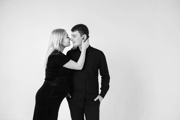 Těhotná žena a její manžel se usmívají v černých šatech na bílém pozadí. Černobílý obrázek. Krásný manželský pár. Kopírovat, prázdné místo pro text. - Fotografie, Obrázek