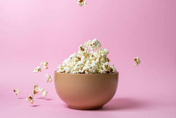 Popcorn on a pink background. A full plate of popcorn. Popcorn falls down. Movie snack. - 写真・画像