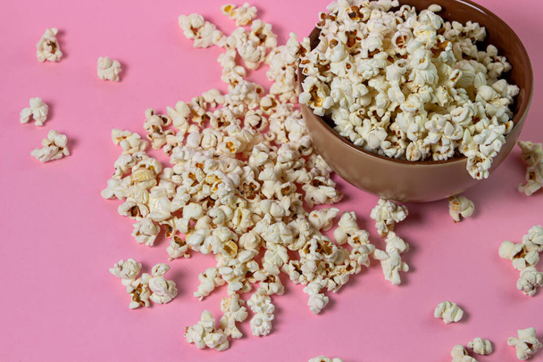 Popcorn on a pink background. A full plate of popcorn. Popcorn is scattered around. Movie snack - Φωτογραφία, εικόνα
