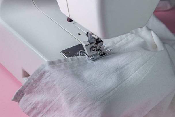 Witte naaimachine op een roze achtergrond. Elektrische naaimachine. witte stof op de naaimachine. Handgemaakt gereedschap. Naaiwerk. - Foto, afbeelding