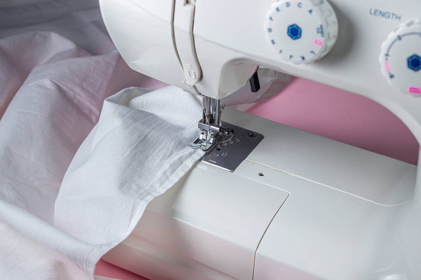 Máquina de coser blanca sobre fondo rosa. Máquina de coser eléctrica. tela blanca en la máquina de coser. Herramienta hecha a mano. Negocios de costura. - Foto, Imagen