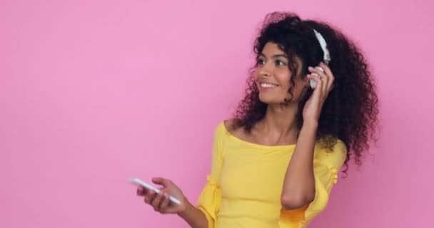 χαρούμενη γυναίκα με ακουστικά που χορεύει και κρατά το smartphone απομονωμένο σε ροζ - Πλάνα, βίντεο