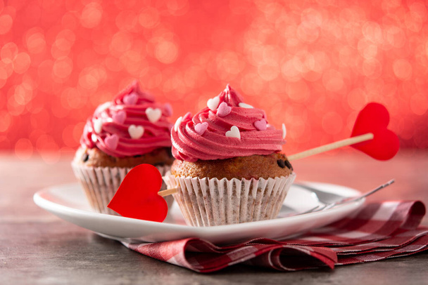 Cupcake decorated with sugar hearts for Valentine's Day on wooden table and red background - Photo, Image