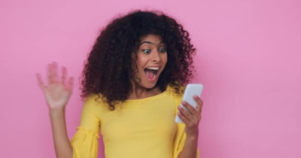 užaslá mladá žena při pohledu na smartphone izolované na růžové - Záběry, video