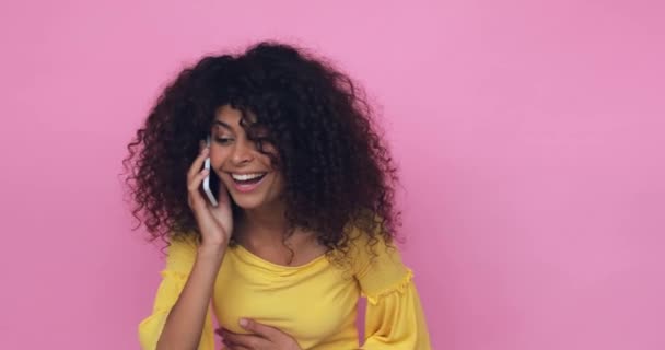 örömteli fiatal nő gesztikulál, miközben beszél okostelefon elszigetelt rózsaszín - Felvétel, videó