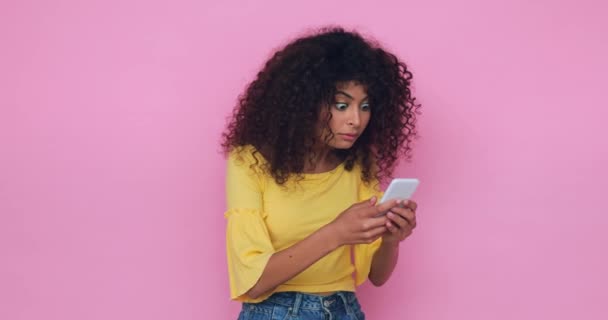 šokovaná mladá žena zprávy na smartphone izolované na růžové - Záběry, video