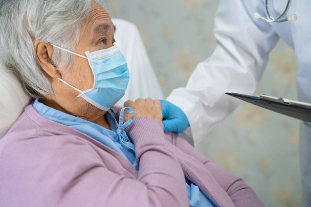Médico que usa estetoscopio para revisar a una paciente asiática de edad avanzada o anciana que lleva una máscara facial en el hospital para proteger la infección Covid-19 Coronavirus. - Foto, imagen