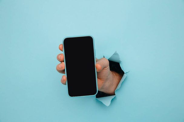 Pánská ruka drží telefon z modrého roztrhaného papíru - Fotografie, Obrázek