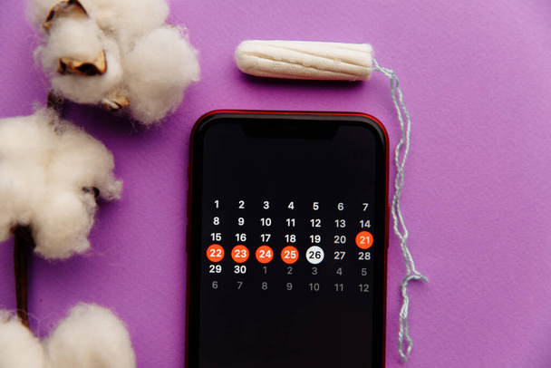 Menstruation calendar in smartphone with cotton and tampon. Woman critical days and hygiene protection concept - Photo, Image