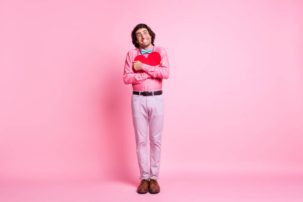 Full length photo of handsome happy guy hug red paper heart beaming smile isolated on pink color background - Фото, зображення