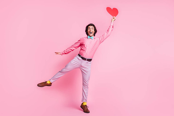 Full size photo of handsome excited young man fly hold paper heart wear glasses blue bowtie isolated on pink color background - Fotoğraf, Görsel