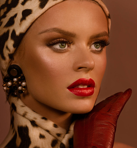 Female portrait. Face close-up. Hat and scarf in a leopard pattern. Large earrings in the ears. Red lipstick. - Fotografie, Obrázek