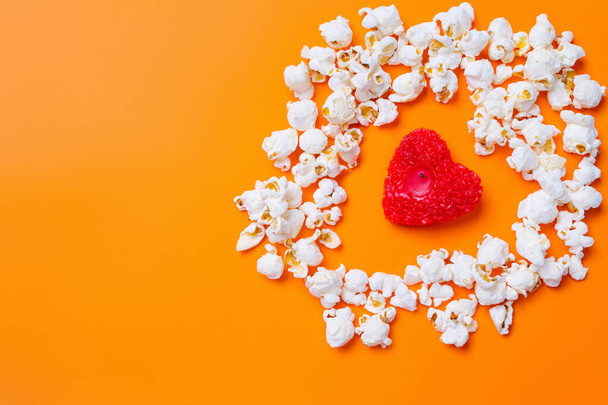  Popcorn and a candle in the shape of a red heart on orange background with blank space. - Foto, Bild