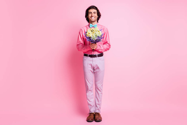 Full size photo of brown haired charming man hold bloom flowers isolated on pastel pink color background - 写真・画像